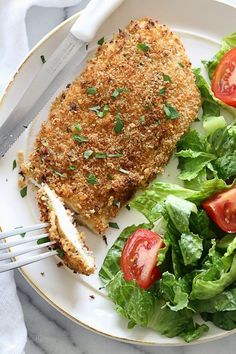 a white plate topped with meat and salad next to a fork on top of a table