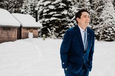 a man in a blue suit is standing in the snow near some trees and houses