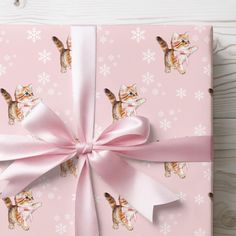 a pink wrapping paper with kittens and snowflakes on it, tied to a wooden table