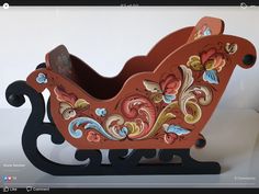 a wooden toy sleigh with flowers painted on the front and sides, sitting on a white surface