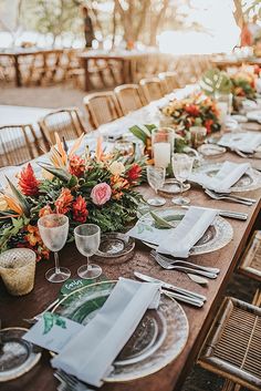 a long table set with place settings and flowers on it for an outdoor dinner party