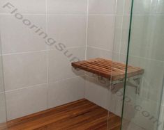 a wooden shelf sitting in the corner of a bathroom next to a glass shower door