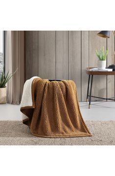 a brown and white blanket sitting on top of a rug next to a table with a potted plant