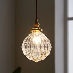 a clear glass light hanging from a cord in front of a white wall and window