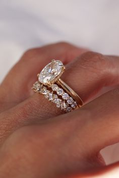 a woman's hand with two gold rings on top of her wedding band and an engagement ring in the middle