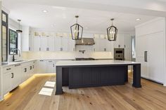 a large kitchen with white cabinets and black island in the center, surrounded by wood flooring