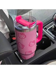 a pink hello kitty cup sitting on top of a car dashboard