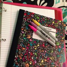 two pens sitting on top of a binder next to a notepad and pen