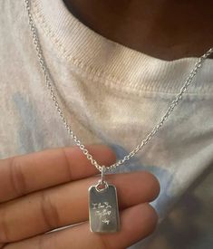 a person holding a silver dog tag on a chain