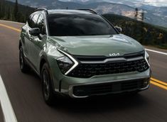 a green suv driving down the road with mountains in the background