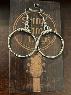 pair of silver colored hoop earrings on top of a wooden table with an advertisement for stringing strings