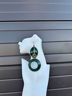 a white mannequin head with green and black earrings hanging from it's side