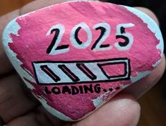 a hand holding a pink painted rock with the words loading on it