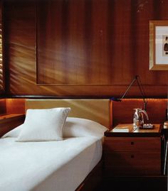 a bed with white sheets and pillows in a room that has wood paneling on the walls