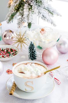 a cup of hot chocolate with marshmallows and christmas decorations around it on a table