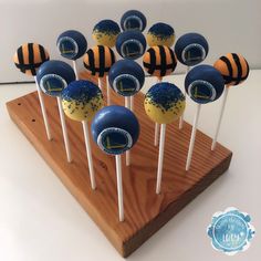 cake pops with blue and yellow frosting are arranged on a wooden stand in front of a white wall