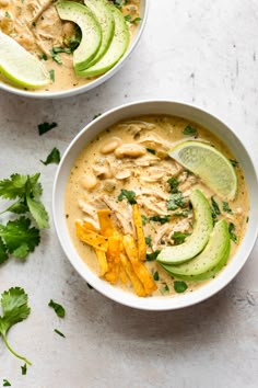 two bowls filled with soup and garnished with avocado wedges on the side