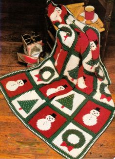 a crocheted christmas afghan with santas and snowmen on it, sitting on a wooden floor