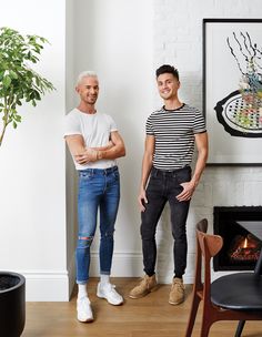 two men standing next to each other in front of a fireplace with a potted plant