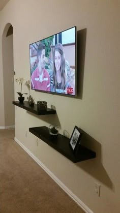 a flat screen tv mounted to the side of a wall next to a shelf with pictures on it