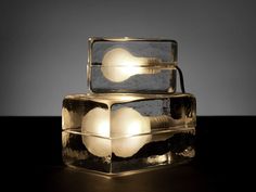 two light bulbs sitting on top of each other in an ice block style container with glass sides