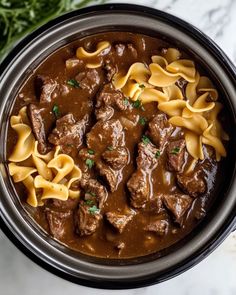 a bowl filled with beef and noodles on top of a marble countertop next to some parsley