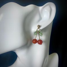 Add a playful touch to your look with these handmade Red Carnelian Cherry Earrings. These delightful earrings feature vibrant red carnelian beads shaped like cherries, complemented by delicate acrylic green leaf accents. The combination of the deep red and fresh green creates a charming and unique design that's perfect for any occasion. Crafted with care and attention to detail, these earrings are a wonderful addition to any jewelry collection. Features: - High-quality gold colored stainless steel earrings - Genuine 8mm red carnelian beads - Acrylic green leaf charms - Handcrafted with attention to detail - Earring length approximately 1.25 inches - Earring weight approximately 3 grams per earring Embrace the fun and whimsical style of these cherry earrings. They make a perfect gift for fr Red Carnelian Earrings Perfect As A Gift, Red Earrings With Natural Stones In Round Beads, Red Carnelian Teardrop Jewelry, Elegant Cherry Drop Earrings, Cheap Trendy Cherry-colored Earrings, Red Carnelian Earrings With Ear Wire, Trendy Cherry Dangle Earrings, Red Carnelian Pierced Earrings, Red Carnelian Earrings