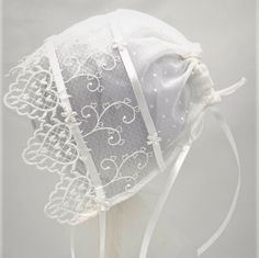 "This pretty bonnet is perfect for all of baby's formal events.  It is made with two layers of sheer fabric, edged with a heart motif lace.  There is a ribbon adjustable back closure and satin ribbon ties.   3-6m      16-18\" 9-12m    18-20\" Hand wash, line dry, cool iron (use a press cloth) All components are CPSIA compliant. All items are made in a smoke and pet free environment." Fitted White Bonnet With Lace Trim, Elegant Lace Bonnet With Lace Trim, Adjustable Lace Wedding Bonnet, Fitted White Bonnet For Baptism, White Fitted Bonnet For Baptism, White Fitted Hat With Lace Trim, White Adjustable Lace Bonnet, White Lace Adjustable Bonnet, Adjustable Cream Bonnet For Baptism