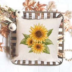 a sunflower pillow sitting on top of a chair next to fall leaves and pumpkins