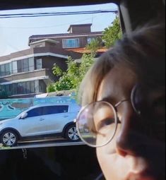 a woman wearing glasses looking out the window at cars parked in front of her house