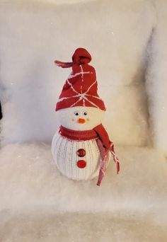 a knitted snowman sitting on top of a white chair with a red hat and scarf