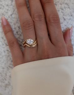 a woman's hand wearing a gold ring with a white diamond on the middle