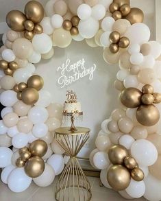 a white and gold birthday cake surrounded by balloons in the shape of a circle on a table