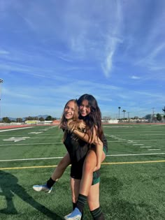 two girls hugging each other on a football field with the sky in the back ground