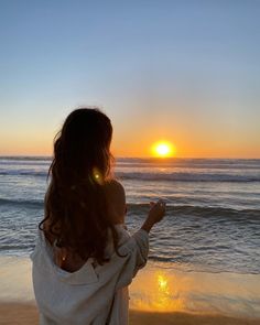 a woman standing on top of a sandy beach next to the ocean at sunset or sunrise