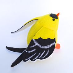 a small yellow bird with black feathers on it's head and tail, sitting on a white surface