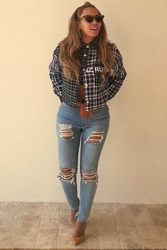 a woman standing in front of a white wall wearing ripped jeans and a plaid shirt