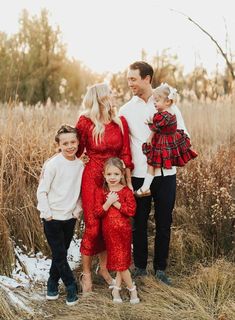 a family posing for a photo in front of some tall grass and trees with snow on the ground