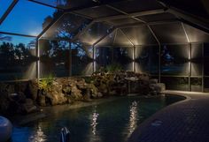 an indoor swimming pool at night with lights on the walls and rocks in the water