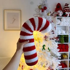 a person holding up a red and white knitted christmas stocking in front of a tree