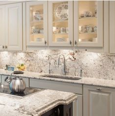 a kitchen with white cabinets and marble counter tops, tea pot on the sink in front of an oven