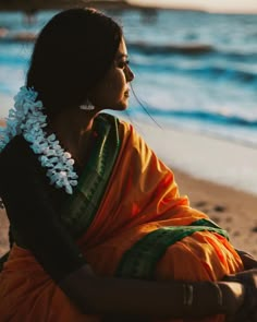 a woman sitting on top of a sandy beach next to the ocean with flowers in her hair