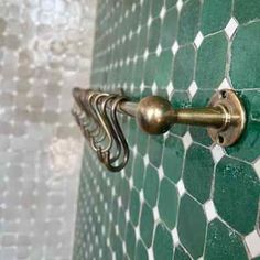 a green and white tiled bathroom with brass handles on the shower door handle, which is attached to an ornately designed tile wall