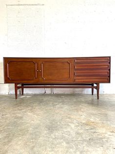 a large wooden sideboard sitting on top of a cement floor next to a white wall