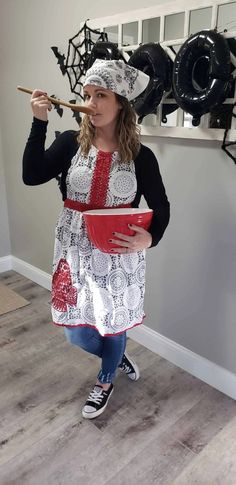 a woman in an apron holding a bowl and chopstick while standing next to a wall