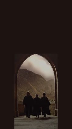 three people standing in front of an arch with mountains in the backgroung