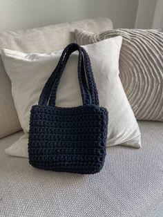 a crocheted bag sitting on top of a couch next to two white pillows