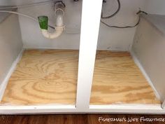 the inside of a white cabinet with wood flooring and piping in between it