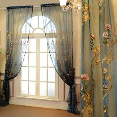 a window with blue curtains and flowers on the windowsill, in front of a chandelier