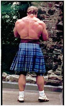 a man in a kilt standing on the side of a road with his back to the camera